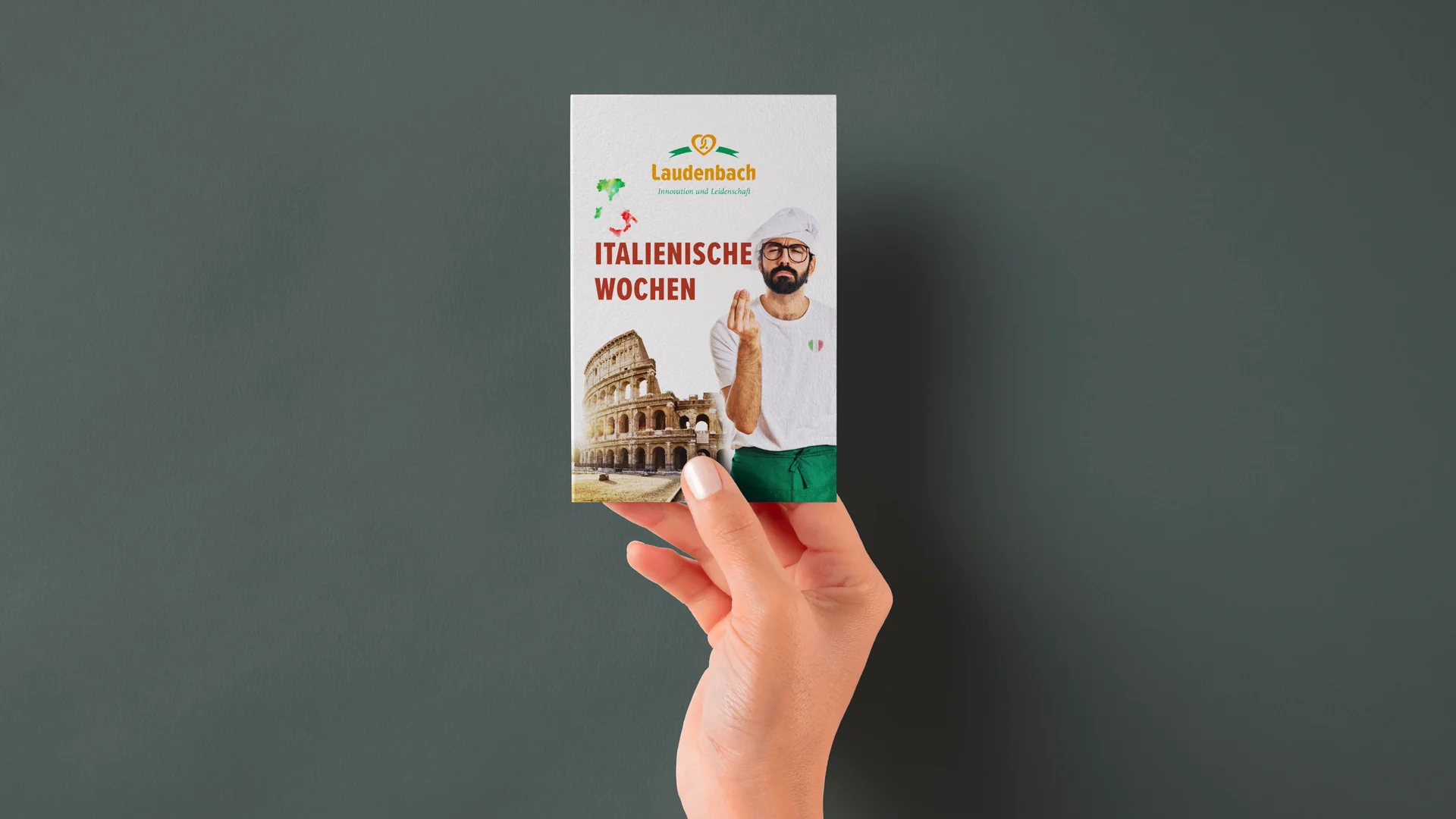 Hand hält Hangtag der Bäckerei Laudenbach für die Italienischen Wochen mit italienischem Bäcker und Kolosseum-Motiv.