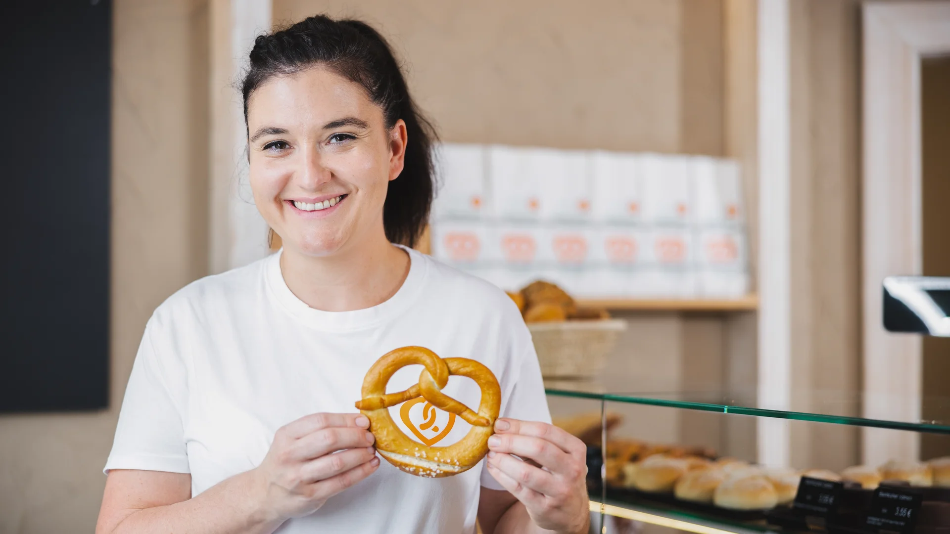 Mitarbeiterin der Bäckerei Laudenbach hält eine Brezel mit Logo im Verkaufsraum