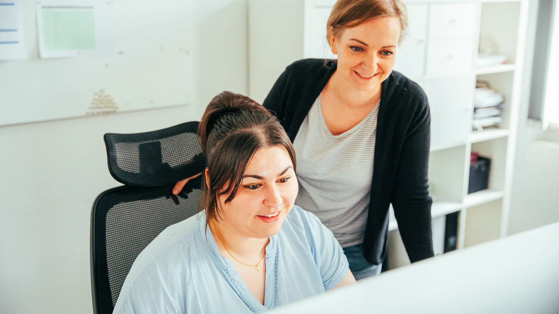 Zwei Kolleginnen von Trendsetzer stimmen sich bei der Arbeit am Bildschirm ab – offene Kommunikation und enge Zusammenarbeit im Marketing-Team.
