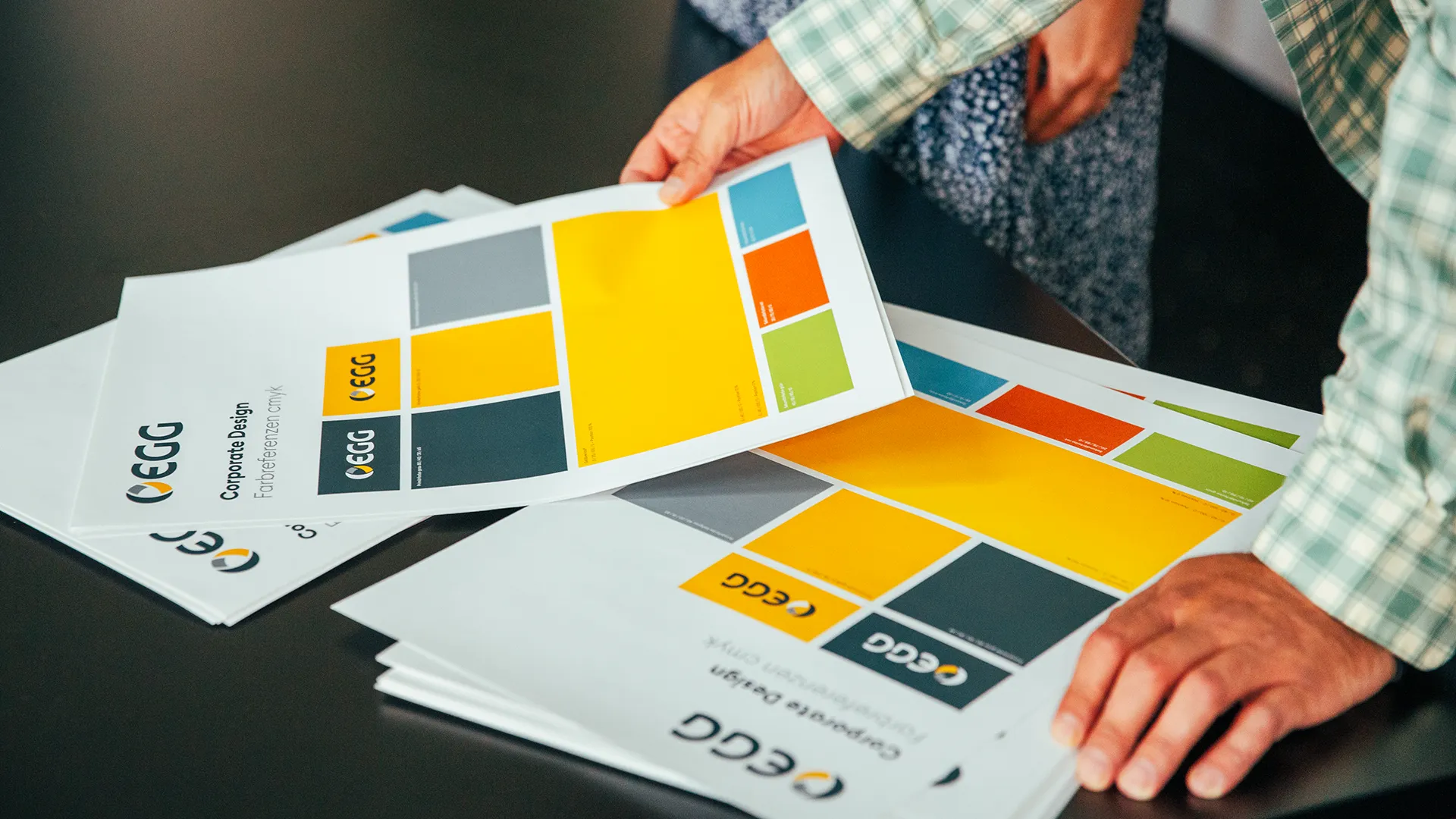 Person betrachtet Andruckbögen mit Farbflächen für das Corporate Design der EGG – professionelle Gestaltung und Farbdefinition.