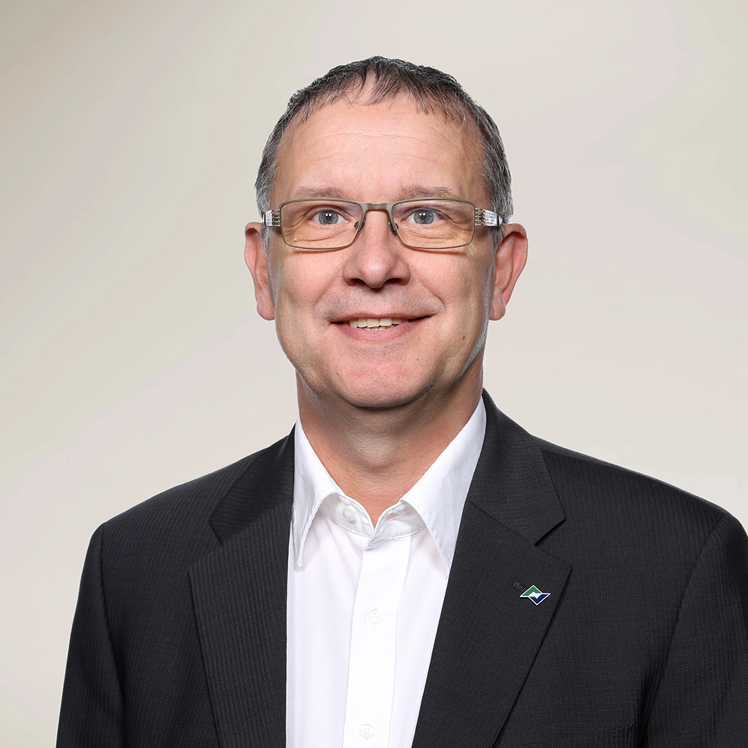 Porträtfoto von Geschäftsführer Stephan Hubrich im dunklen Anzug mit weißem Hemd, freundlich lächelnd vor hellem Hintergrund.
