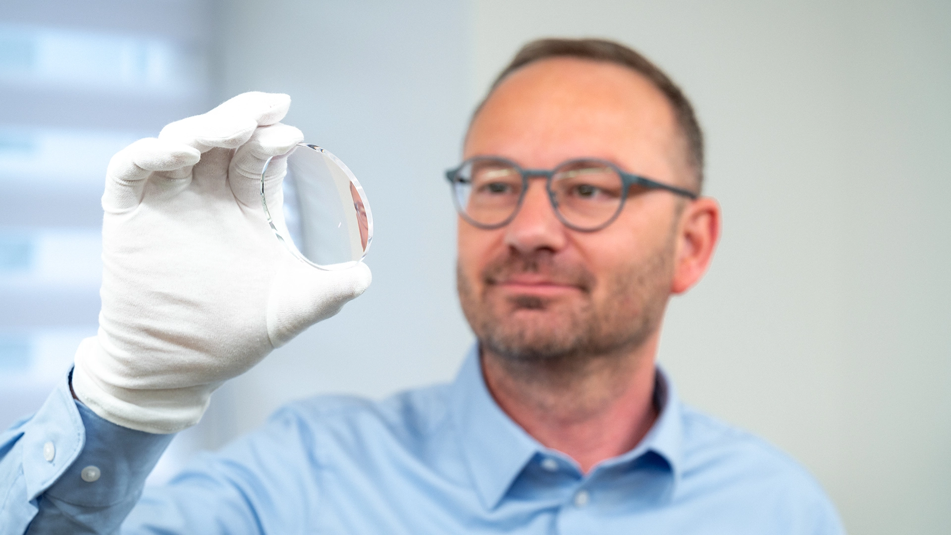 Mann mit Brille und Handschuh hält präzise geschliffenes Brillenglas bei einem Sachsenweger-Imageshooting.