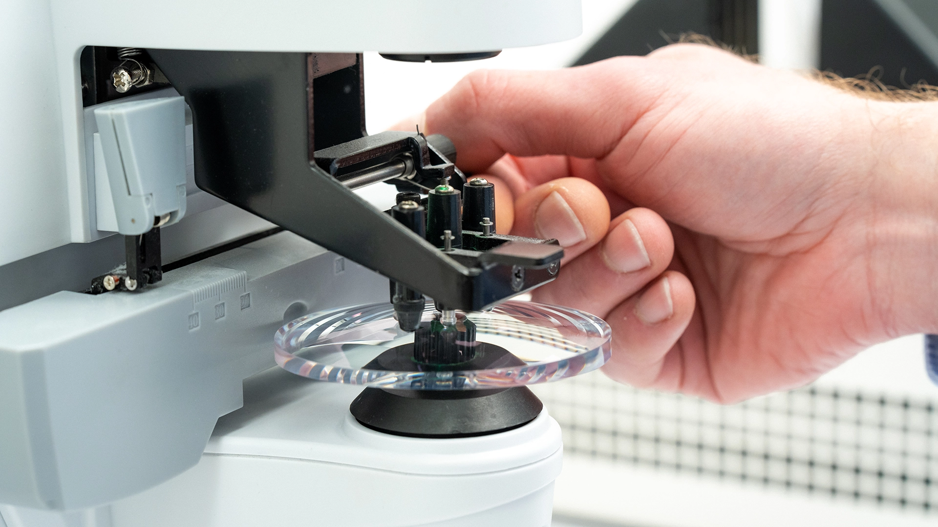 Hand setzt ein Brillenglas präzise in eine Maschine ein, Detailaufnahme aus der Sachsenweger-Produktion.