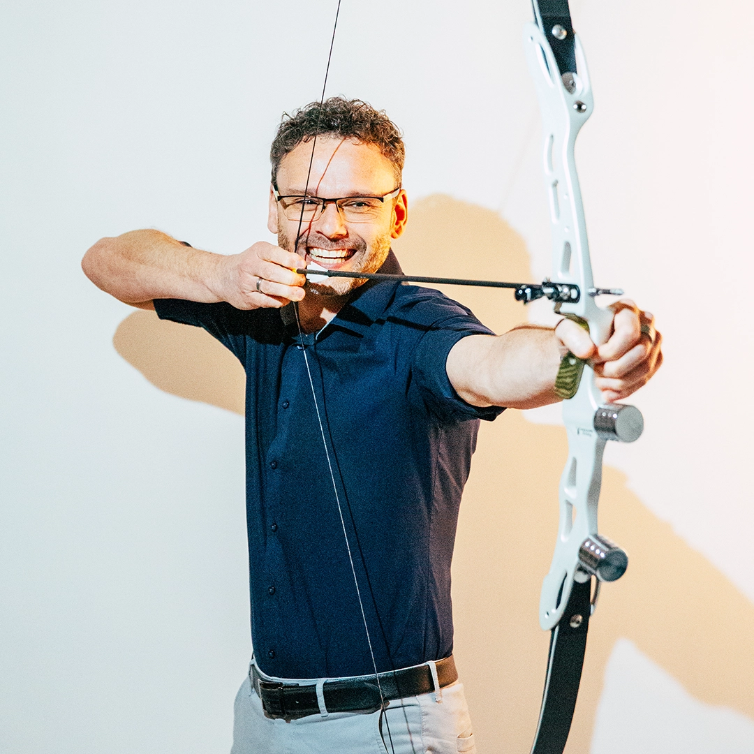 Mitarbeiterfoto von Sebastian Uebel, Geschäftsführer Design bei Trendsetzer, mit gespanntem Bogen – kreative Visualisierung von Fokus und Zielstrebigkeit.